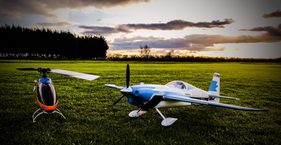 A model helicopter and an aerobatic model aircraft on the grass at Langar at sunset